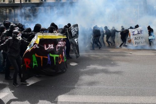 La gente tiene gli striscioni di protesta mentre marcia tra il fumo dei lacrimogeni durante gli scontri di Parigi