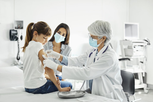 Girl receiving COVID-19 shot and looking at her arm.